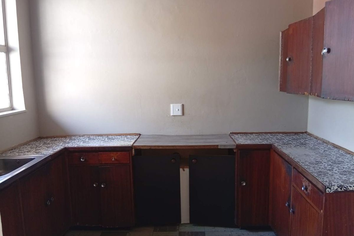 A dated kitchen featuring original wooden cabinetry, laminate countertops, and a stainless steel sink, offering a blank canvas for a modern renovation.
