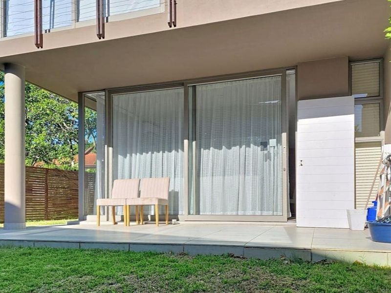 A covered ground-floor patio featuring large sliding glass doors, tiled flooring, and direct access to a private garden area.