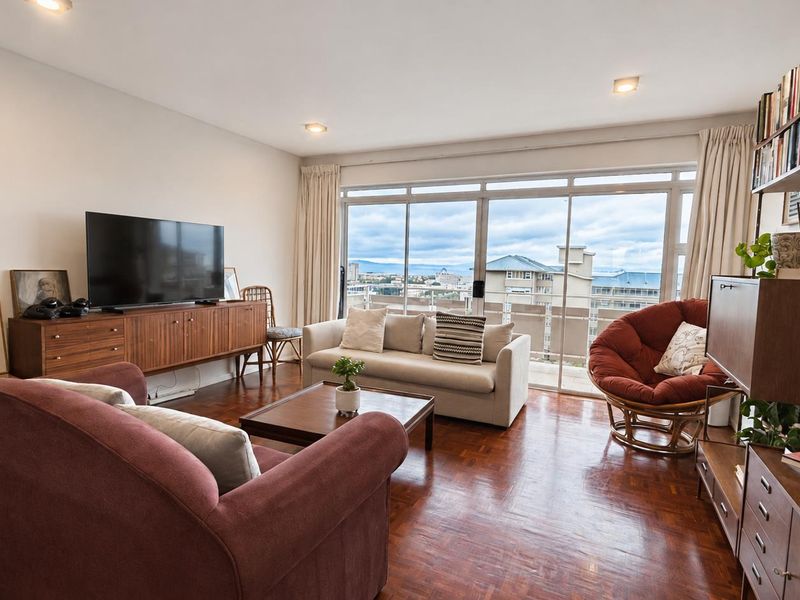 A bright living room featuring warm parquet flooring, recessed lighting, and large sliding glass doors that open to a balcony with city views.