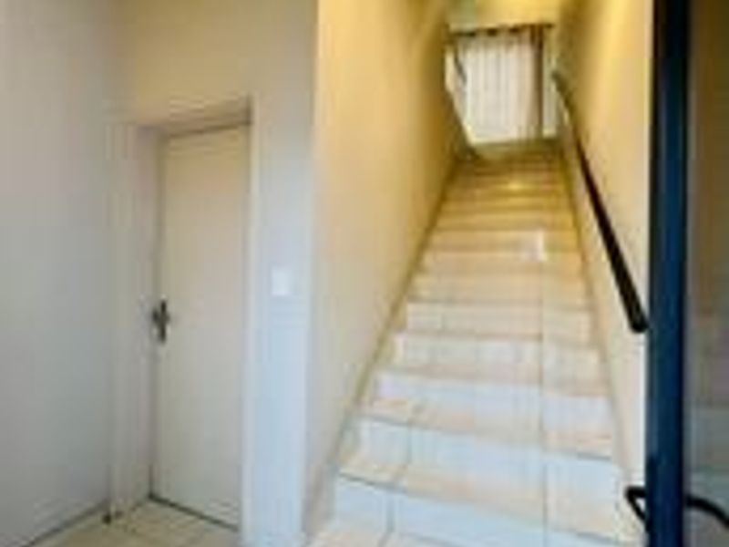 A bright entrance area featuring a tiled staircase with a handrail, leading to an upper level.