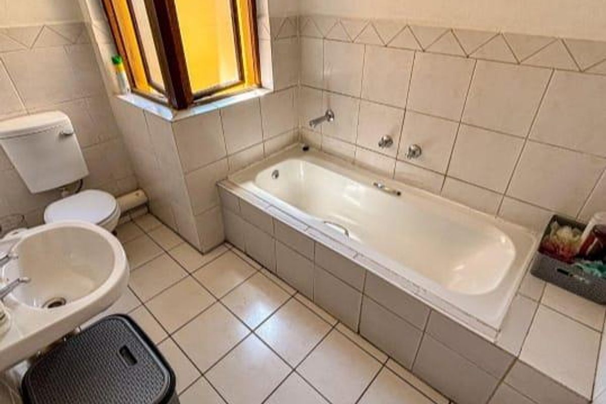 A functional bathroom featuring a built-in bathtub with tiled surround, a pedestal basin, and a standard toilet, finished with neutral ceramic wall and floor tiles.