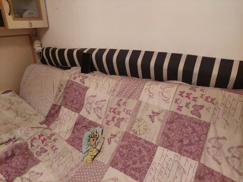 A bedroom interior featuring a built-in headboard, showing signs of wear on the surrounding wall surfaces.