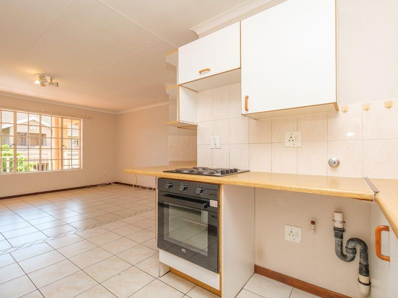 Open-plan kitchen and living area featuring tiled flooring, built-in cabinetry, and a fitted oven and hob, offering a functional blank canvas for renovation.