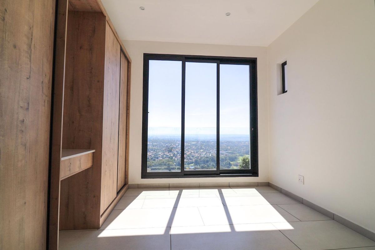 A bright, modern bedroom featuring built-in wooden cabinetry, large sliding glass doors, and expansive elevated views of the surrounding area.