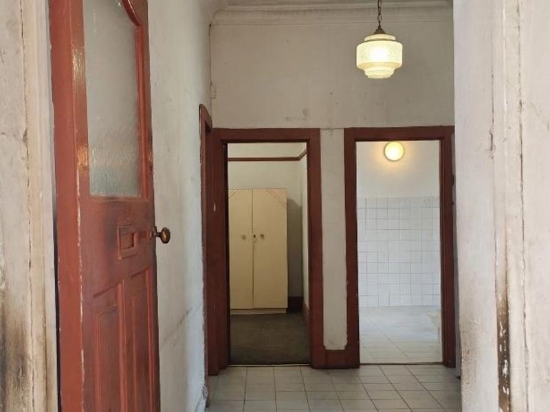 A dated interior hallway featuring tiled flooring, timber door frames, and access to adjacent rooms, requiring cosmetic updates and fresh paint.