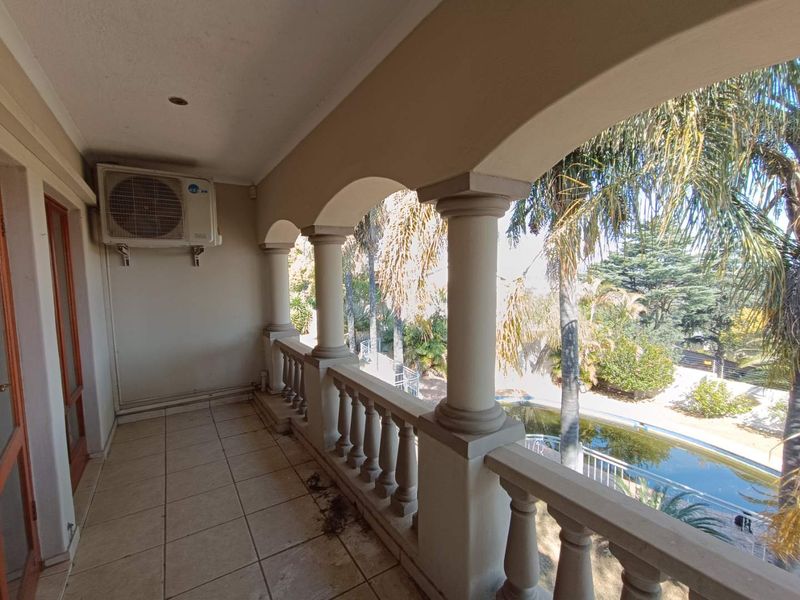 Covered balcony featuring classic columns, a balustrade, and tiled flooring, overlooking the garden and pool area.
