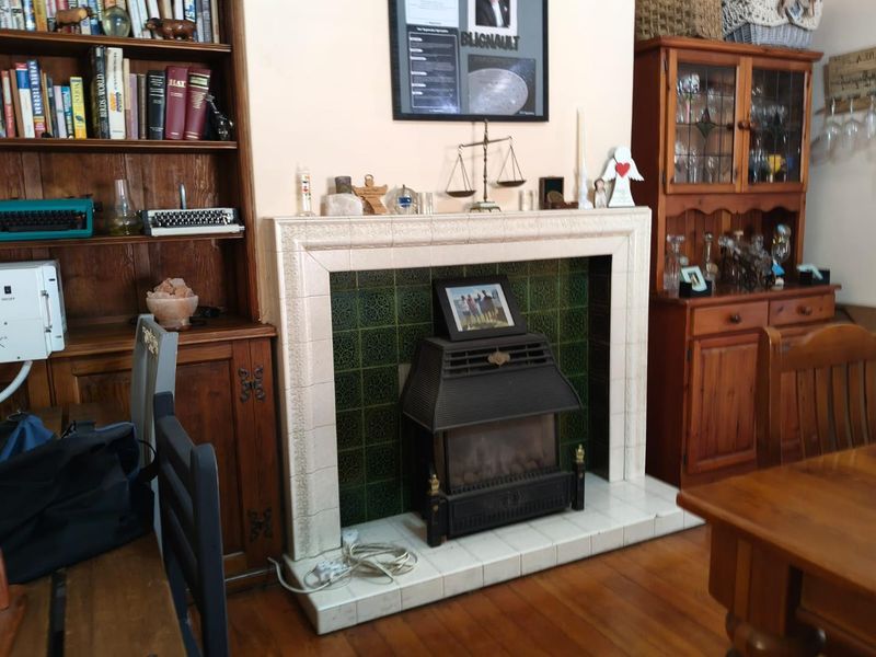 A living room featuring a traditional fireplace with decorative green tiles and a built-in timber bookshelf and display cabinet.