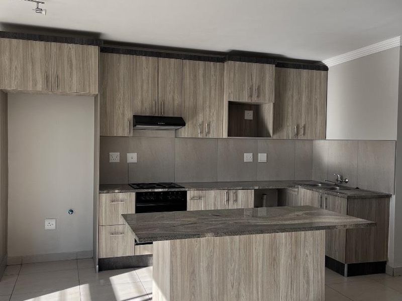 Modern kitchen featuring wood-grain cabinetry, stone countertops, a central island, and built-in appliances, offering a clean and functional workspace.