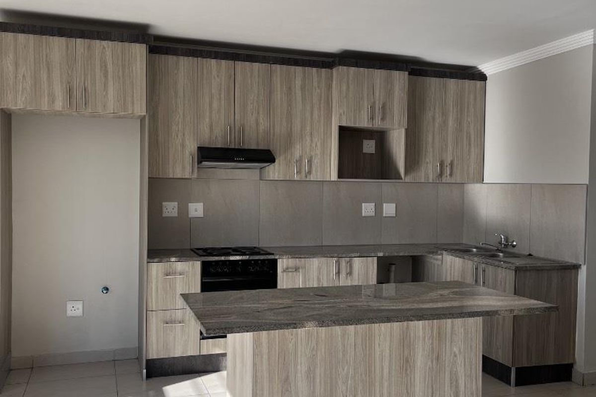 Modern kitchen featuring wood-grain cabinetry, stone countertops, a central island, and built-in appliances, offering a clean and functional workspace.