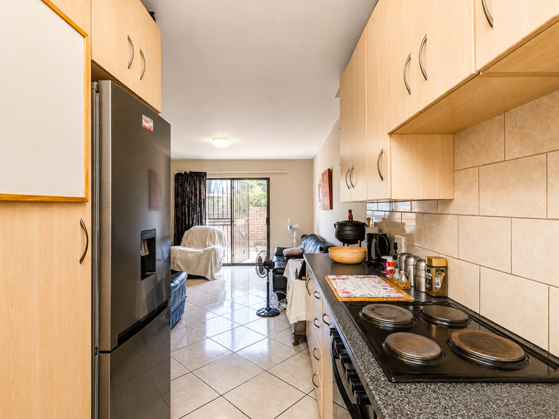 Open-plan kitchen and living area featuring light wood cabinetry, tiled flooring, and a sliding door leading to an outdoor space.