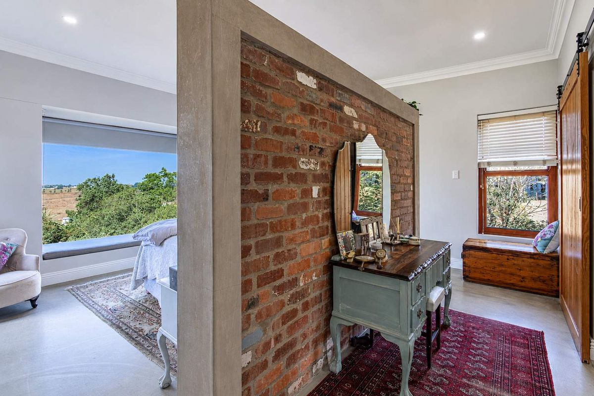 Spacious bedroom featuring a central exposed brick partition wall, a built-in window seat with scenic views, and a sliding barn door.
