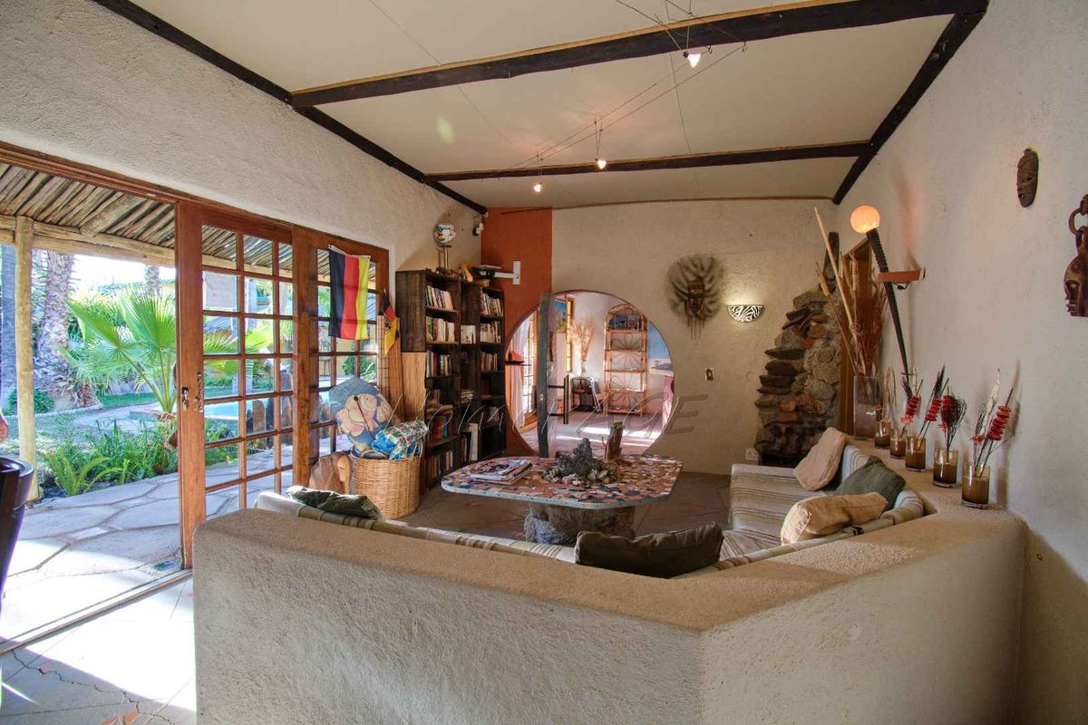 A rustic living room featuring a unique circular doorway, exposed ceiling beams, and large wooden sliding doors opening to a garden patio area.
