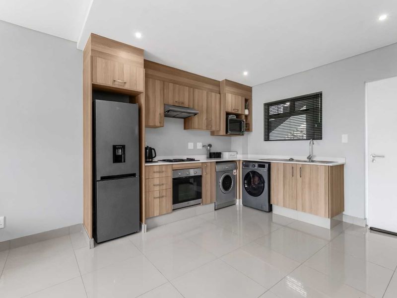 Modern kitchen featuring light wood cabinetry, integrated appliances, sleek countertops, and tiled flooring in a clean, well-lit open space.
