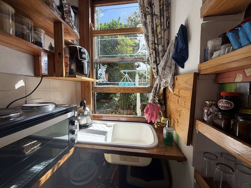 Compact scullery area featuring built-in wooden shelving, a ceramic sink with brass faucet, and a window overlooking the garden.