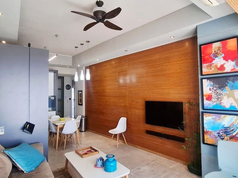 Modern open-plan living area featuring a wood-paneled feature wall, recessed lighting, ceiling fan, and tiled flooring, creating a bright and contemporary space.