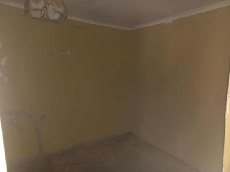An empty bedroom featuring plain walls with visible surface damage and peeling paint, requiring cosmetic renovation and fresh finishes.