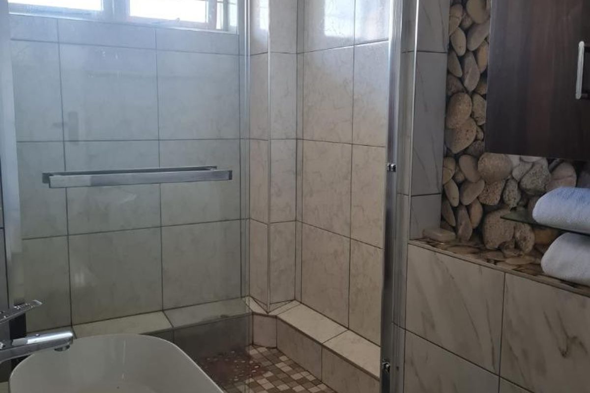 A bathroom featuring a glass-enclosed shower, a modern vessel sink, and a decorative stone feature wall with built-in cabinetry.