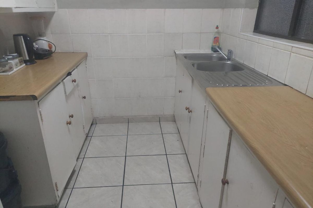A functional kitchen featuring laminate countertops, double bowl stainless steel sink, tiled splashback, and white built-in cabinetry with ceramic floor tiles.