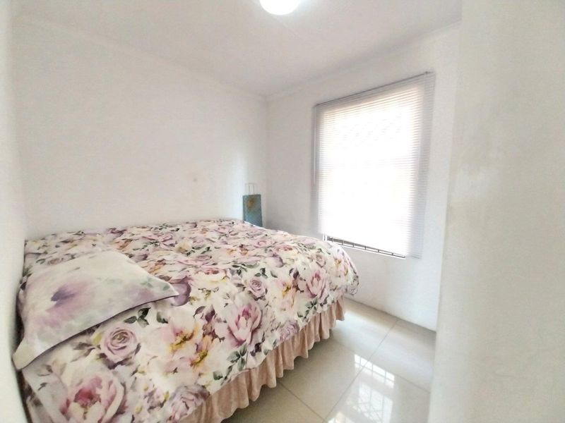 A simple bedroom featuring tiled flooring, neutral walls, and a window fitted with venetian blinds, providing a clean and functional living space.
