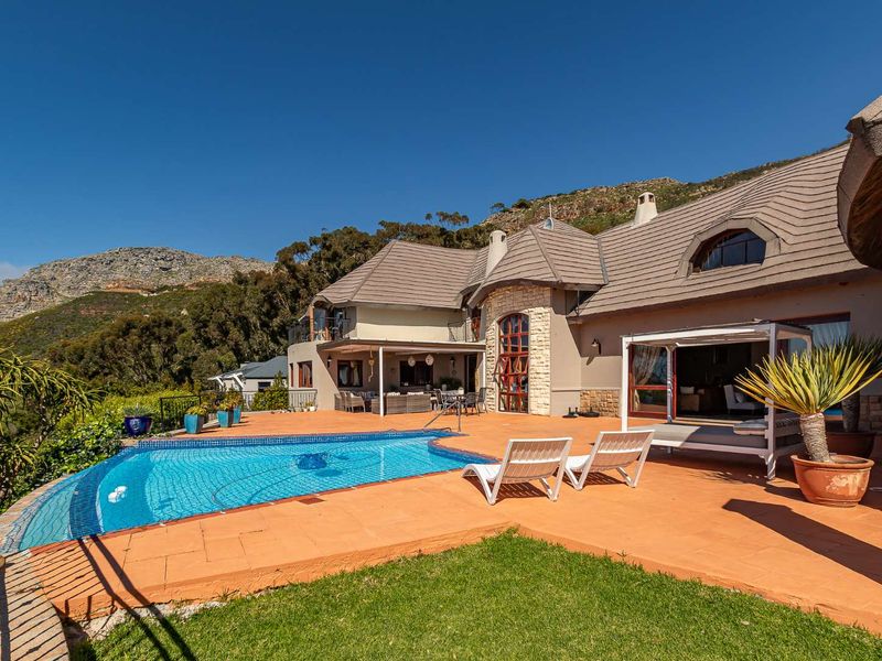 Spacious outdoor pool area featuring a tiled deck, stone-clad architectural details, and a covered patio overlooking the surrounding mountain landscape.