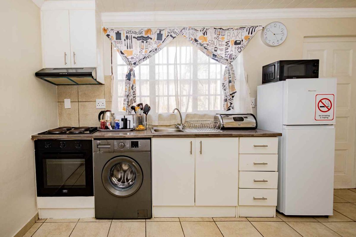 Compact kitchen featuring built-in oven, hob, extractor fan, and integrated laundry plumbing, finished with tiled flooring and laminate countertops.