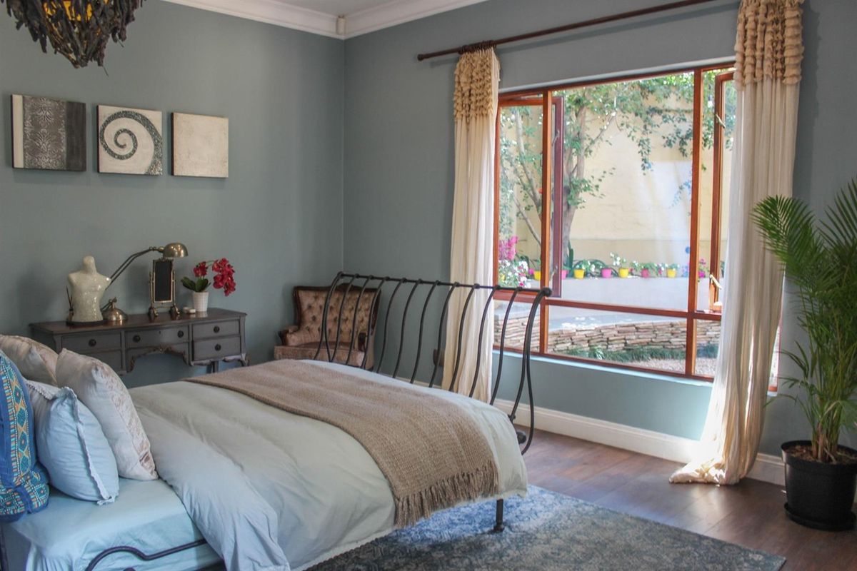 A well-maintained bedroom featuring timber flooring, decorative cornice, and a large window overlooking a garden area.