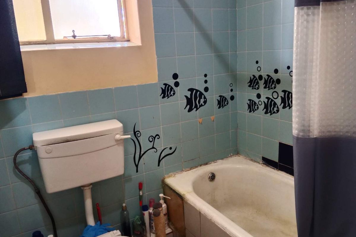 A dated bathroom featuring a standard bathtub, wall-mounted toilet cistern, and light blue wall tiles with decorative decals.