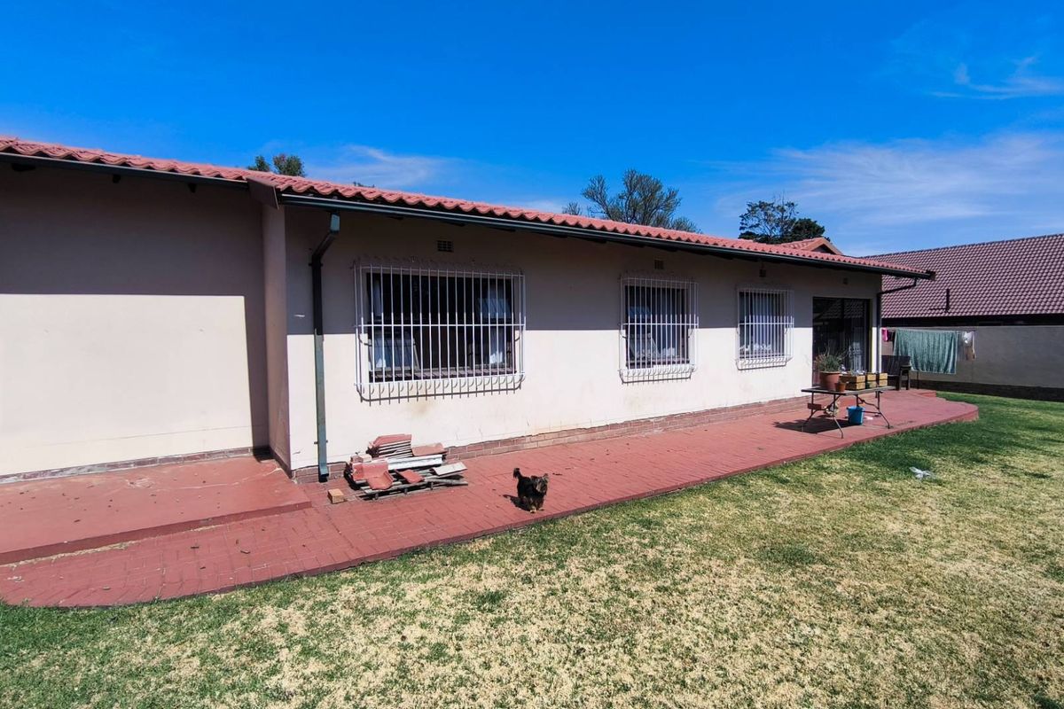 Rear view of the house featuring a tiled roof, security bars on windows, and a paved patio area leading to the garden.