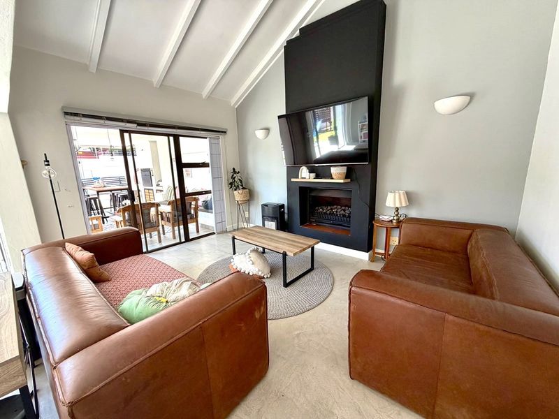 Spacious living room featuring a vaulted ceiling with exposed beams, a modern fireplace, and large sliding glass doors leading to an outdoor patio area.