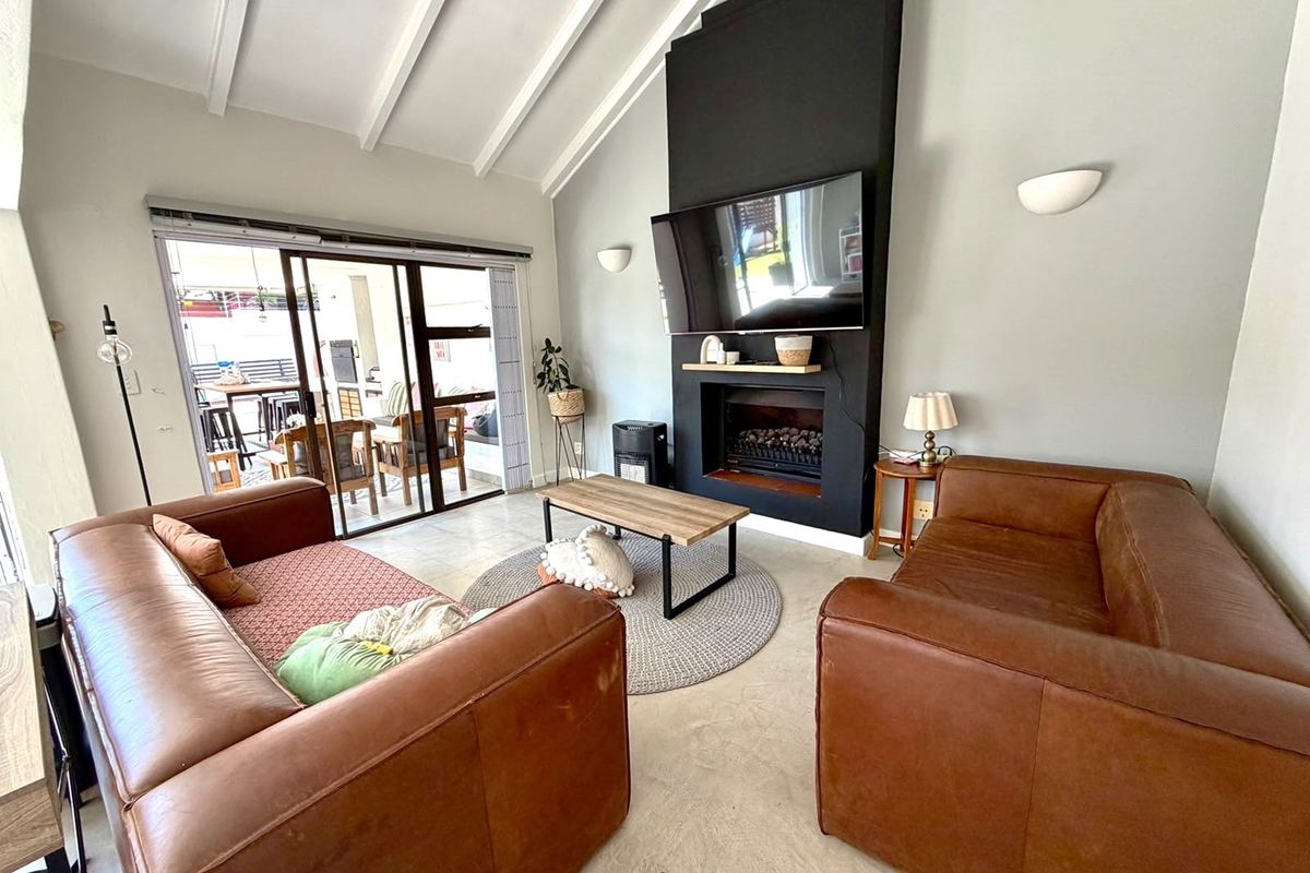 Spacious living room featuring a vaulted ceiling with exposed beams, a modern fireplace, and large sliding glass doors leading to an outdoor patio area.