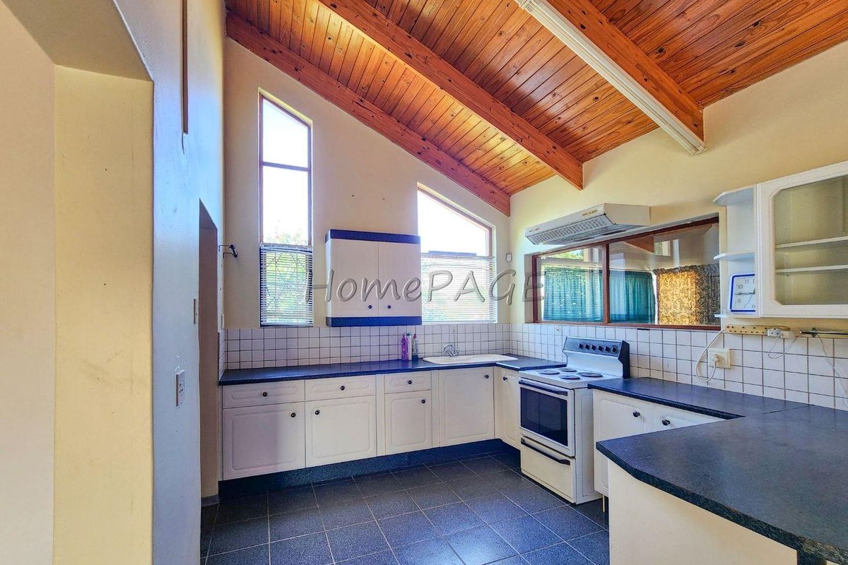 A kitchen featuring a high vaulted timber ceiling, white cabinetry, dark countertops, and tiled flooring, offering a functional layout with ample natural light.
