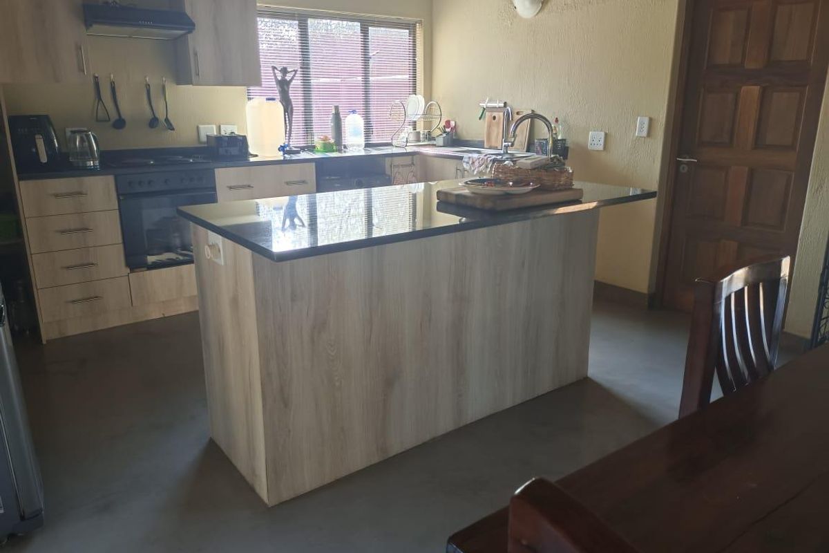 A functional kitchen featuring a central island with granite countertops, light wood-finish cabinetry, built-in oven, and an integrated extractor fan.