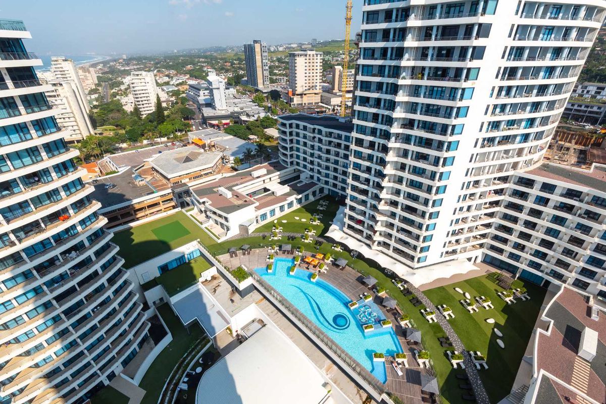 Aerial view of a modern apartment complex featuring a central swimming pool, landscaped garden areas, and surrounding urban infrastructure.