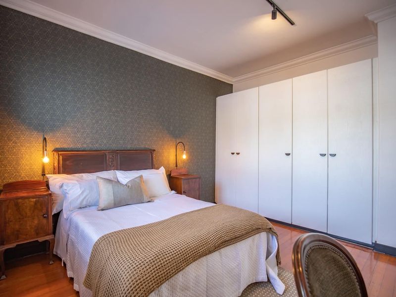 A well-maintained bedroom featuring built-in wardrobes, hardwood flooring, and decorative wallpaper, creating a comfortable and functional living space.