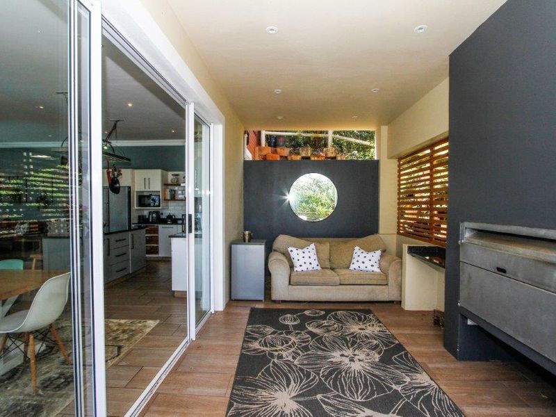 Covered patio area featuring a built-in braai, tiled flooring, and large sliding doors providing seamless access to the open-plan kitchen and dining space.