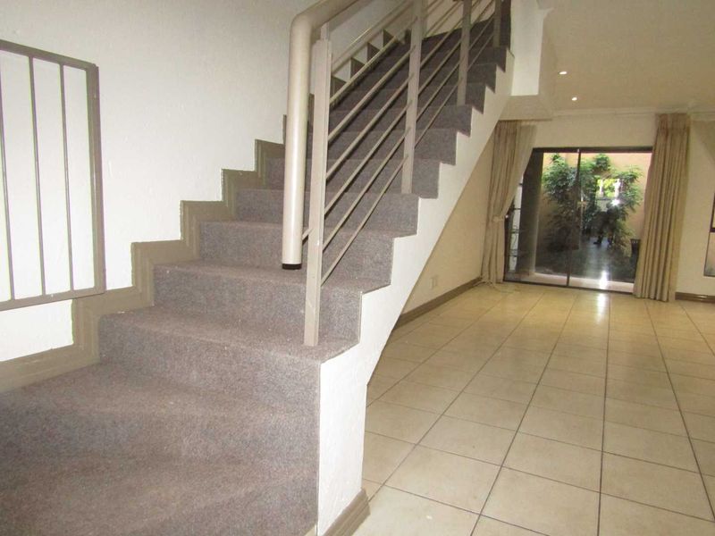 An open hallway featuring a carpeted staircase with a metal handrail, tiled flooring, and a sliding glass door leading to an outdoor area.
