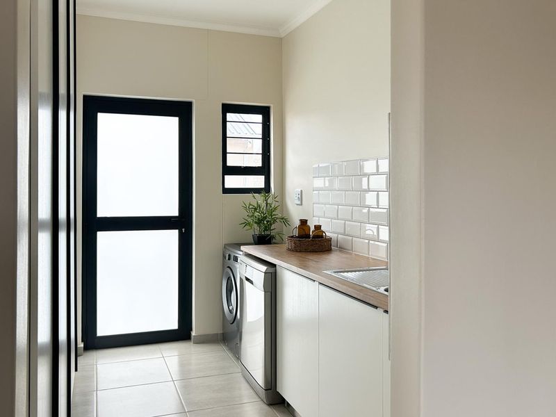 A clean and modern laundry room featuring built-in cabinetry, a wood-look countertop, subway tile backsplash, and a frosted glass exterior door.