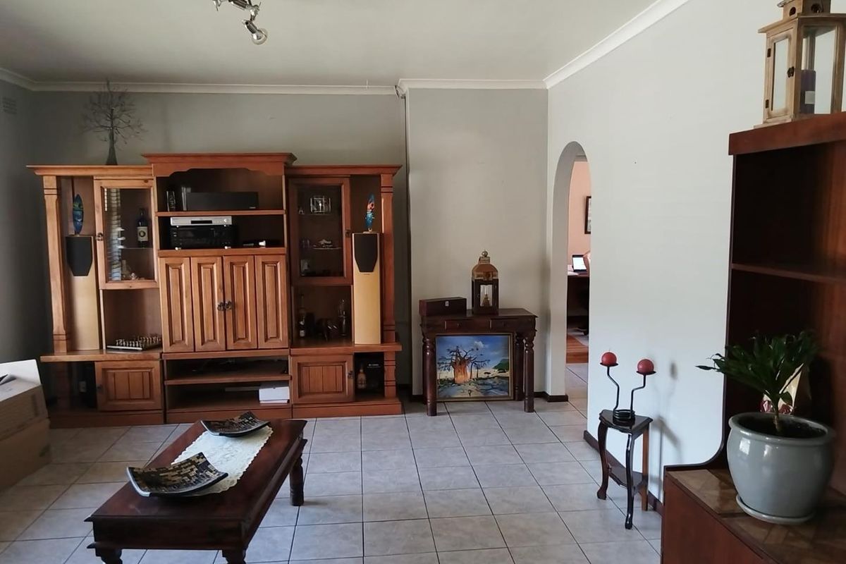 A spacious living room featuring neutral tiled flooring, coved ceilings, and an arched doorway leading to an adjacent room.