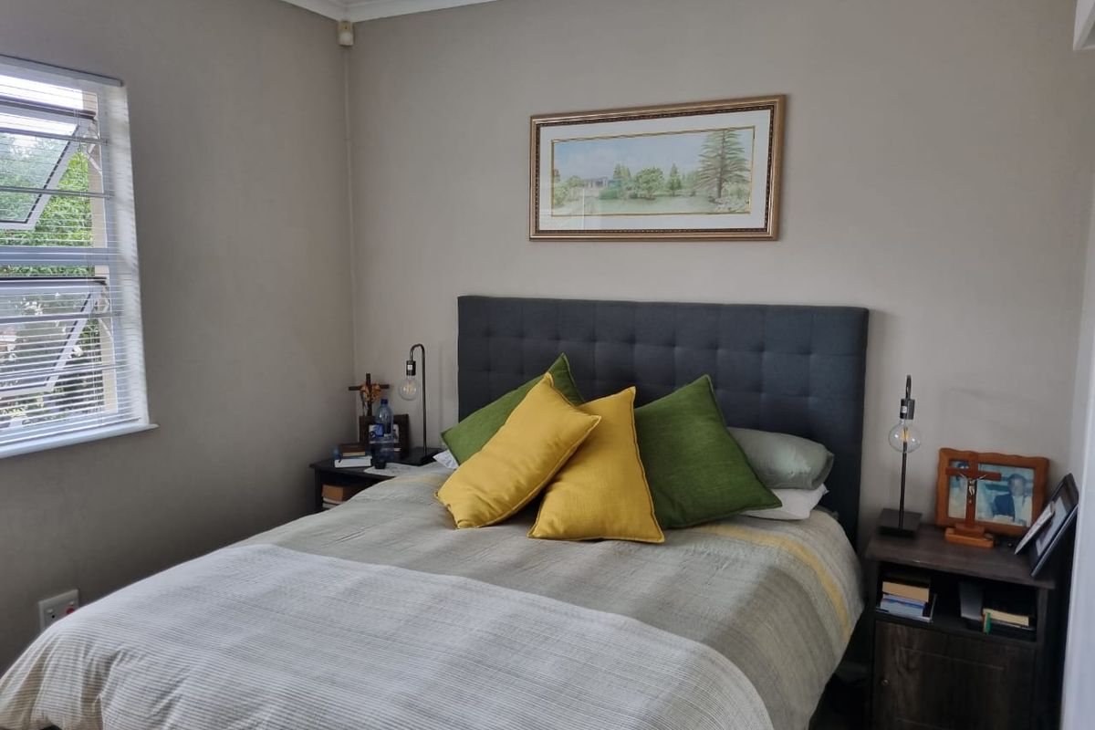 A well-maintained bedroom featuring neutral wall tones, a large window with louvre blinds, and crown molding.