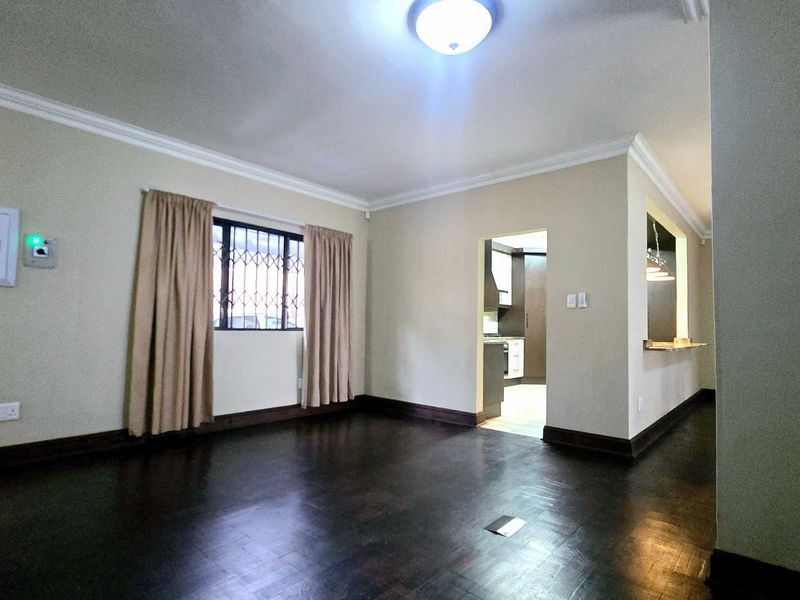 Spacious living area featuring dark parquet flooring, cove cornicing, and a convenient breakfast bar pass-through to the kitchen.
