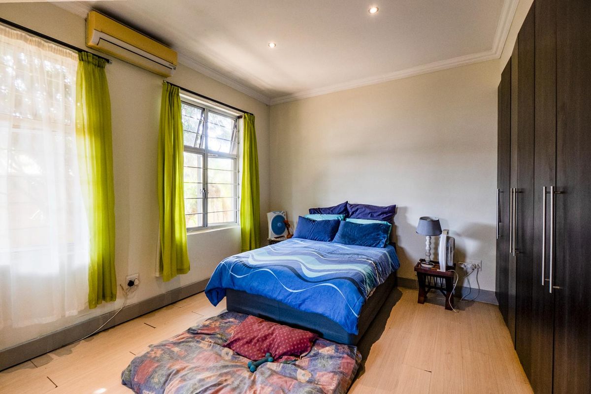 A bedroom featuring built-in dark wood cabinetry, laminate flooring, and a wall-mounted air conditioning unit.