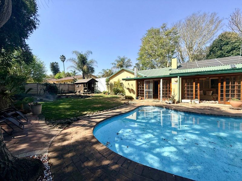 A rear garden featuring a swimming pool with brick coping, solar panels on the roof, and timber-framed glass doors leading into the home.