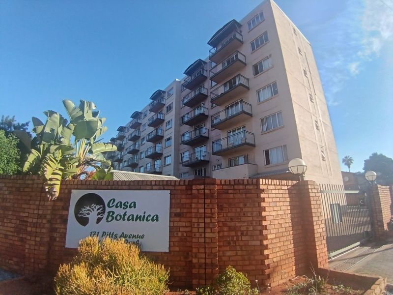 Exterior view of the Casa Botanica apartment complex, featuring a brick boundary wall, security gate, and multiple residential balconies.