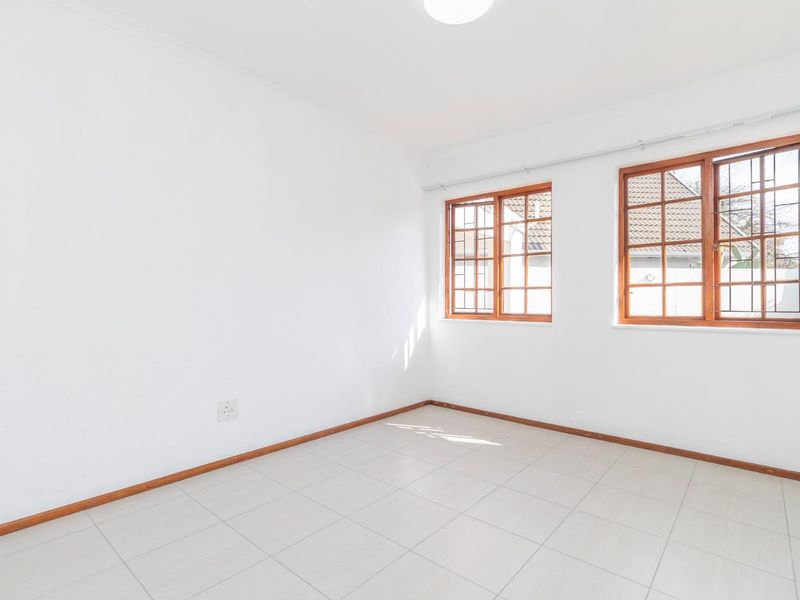 A bright, empty bedroom featuring neutral tiled flooring, white walls, and timber-framed windows with security bars.