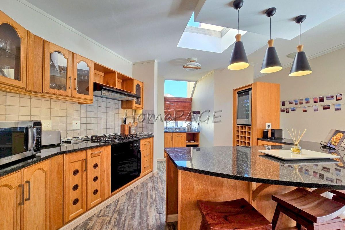A well-lit kitchen featuring wooden cabinetry, granite countertops, a central island, built-in oven, gas hob, and a skylight providing natural illumination.
