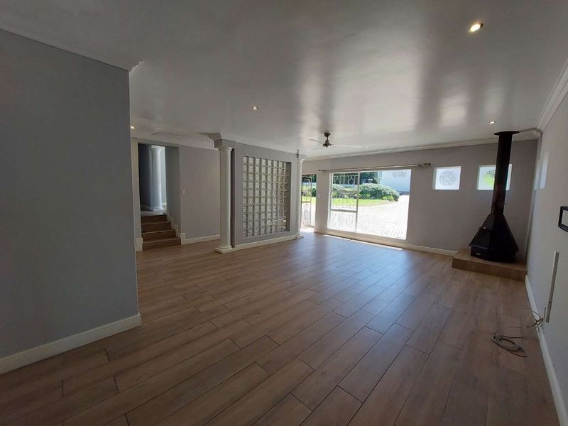 Spacious, light-filled living area featuring wood-look tile flooring, a modern freestanding fireplace, and a unique glass block feature wall.