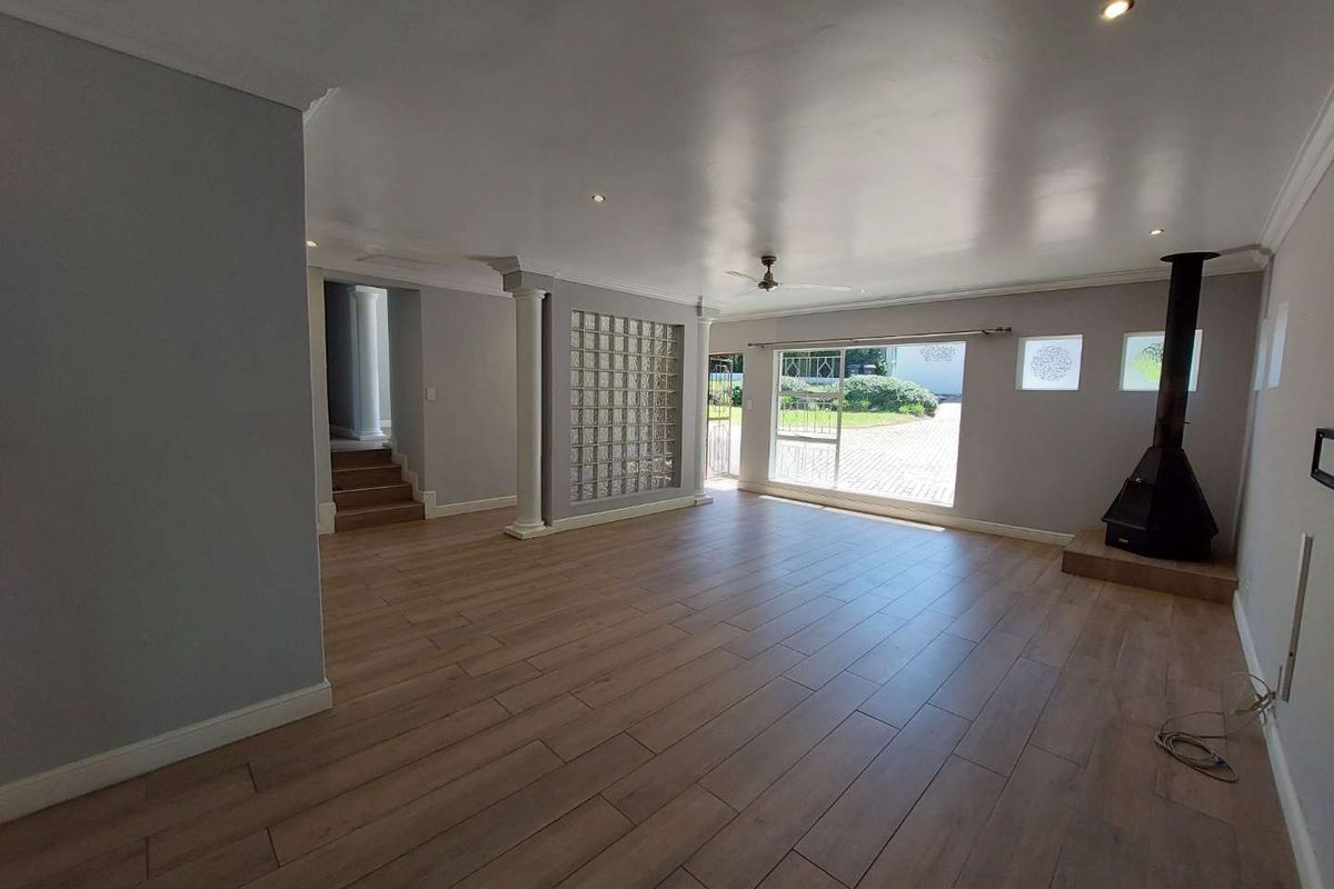 Spacious, light-filled living area featuring wood-look tile flooring, a modern freestanding fireplace, and a unique glass block feature wall.
