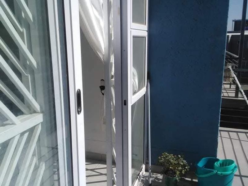 A compact balcony featuring tiled flooring and a sliding glass door with an integrated security gate, providing access to the apartment interior.