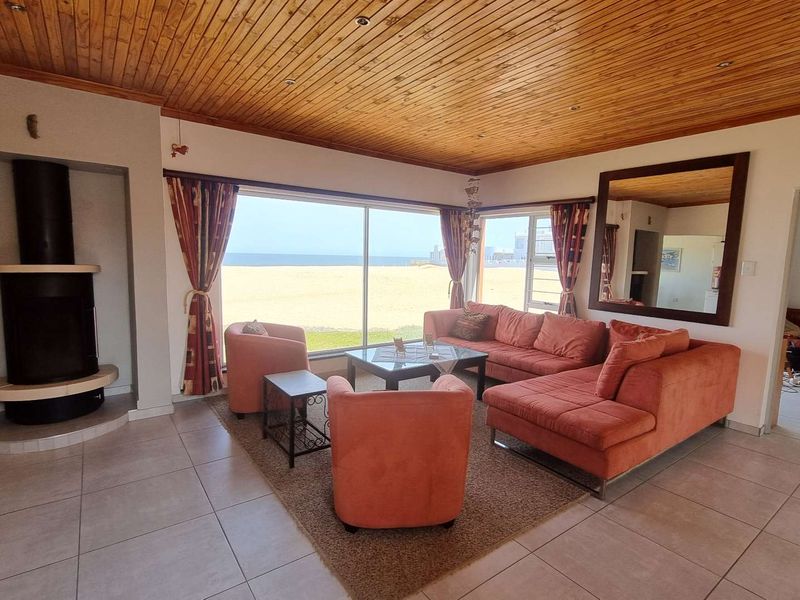 Spacious living room featuring a wood-paneled ceiling, a freestanding fireplace, and large sliding doors offering direct views of the beach.