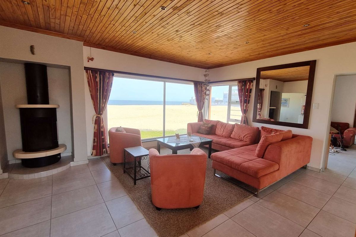 Spacious living room featuring a wood-paneled ceiling, a freestanding fireplace, and large sliding doors offering direct views of the beach.